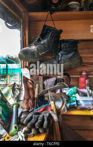 Ein Gartenhaus mit einem Paar schwarze Stiefel, einige im Garten arbeitende Werkzeuge und Saatgut Pakete, neben einem Fenster mit den Kleingärten außerhalb, Stockfoto