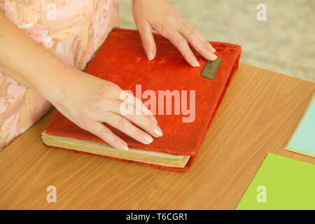 Die Frau legte ihre Hände auf die rote Abdeckung eines Foto Buch oder Album, auf dem Schreibtisch. Die Aussicht von oben. Stockfoto