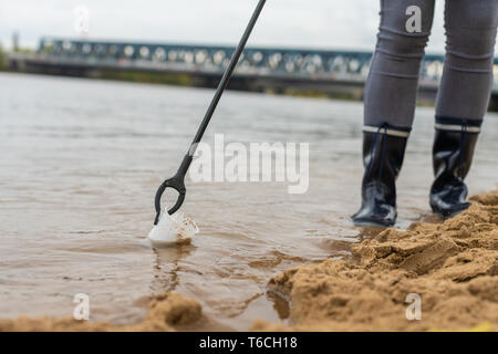 Sammeln von Kunststoffabfällen mit einer Zange vom Strand Stockfoto