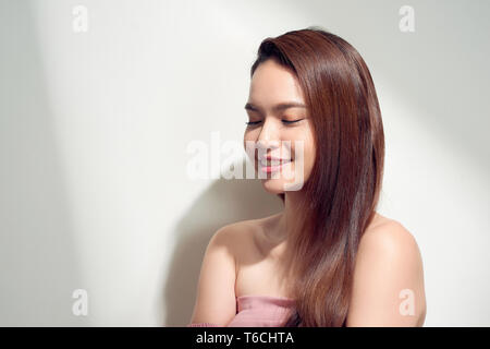 Elegantes asiatisches Mädchen mit gebräunter Haut mit nachdenklichen Gesichtsausdruck auf hellen Hintergrund posiert. Stockfoto