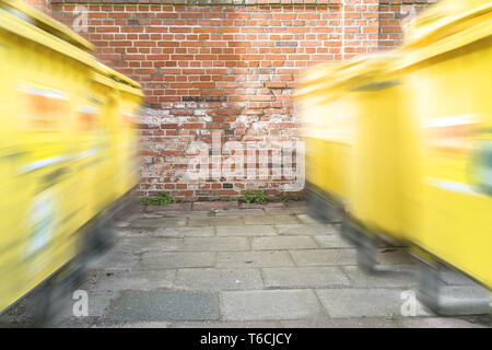 Verschieben von gelb Müllcontainer vor einer roten Backsteinmauer Stockfoto