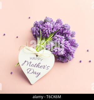 Feder violett Blumen auf Rosa. Eine Herzform tag mit Text einen glücklichen Muttertag. Farben pastell Grußkarte. Stockfoto