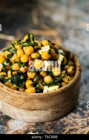 Nahaufnahme eines Kichererbsen Salat, mit gekochtem Spinat, Pinienkerne, Zwiebel und Käse, in einem rustikalen Buchsbaum Schüssel serviert, auf einem rustikalen Tisch Stockfoto