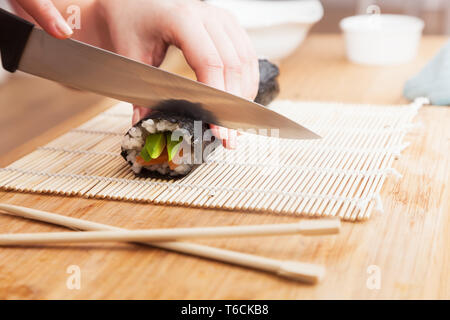 Vorbereitung Sushi, schneiden. Lachs, Avocado, Reis und Essstäbchen auf hölzernen Tisch. Stockfoto