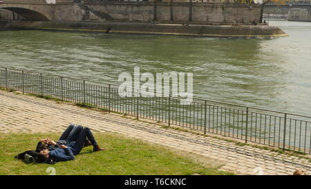 Ein romantisches Paar liegen auf dem Rasen in der Sonne auf dem Ufer der Seine in Paris. Stockfoto