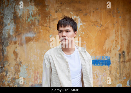 Asiatischer Mann in Freizeitkleidung auf alte Mauer Hintergrund. Stockfoto