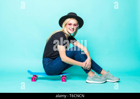 Lächelnde junge Frau sitzt und auf Skateboard über grüne Hintergrund posiert Stockfoto