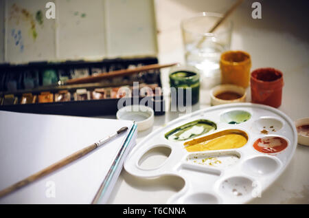 Einstellen der Kunst Zubehör für Zeichnung: Aquarell- und Gouachefarben, Pinsel, Skizzenbuch, Plastik Palette und eine Tasse Wasser für Waschbürsten Stockfoto