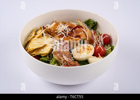 Selektiver Fokus klassische Caesar Salat mit gerösteten Chiken, Speck, Wachteleier, Salatblätter, Chips, Parmesan, Kirschtomaten auf die weiße runde Pla Stockfoto