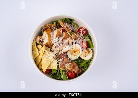 Selektiver Fokus klassische Caesar Salat mit gerösteten Chiken, Speck, Wachteleier, Salatblätter, Chips, Parmesan, Kirschtomaten auf die weiße runde Pla Stockfoto