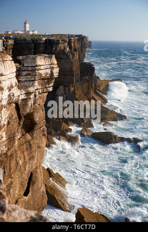 Felsen und Wellen surfen im Meer in der Nähe von Cabo Carvoeiro, Peniche Halbinsel mit dem Leuchtturm im Hintergrund, Portugal Stockfoto