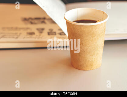 Kaffee in einem recyclingfähigem Papier einweg Glas mit einem offenen Notebook im Hintergrund. Erholsamen Urlaub und Umwelt schützen Stockfoto