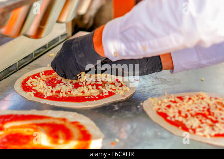 Pizzabäcker Vorbereitung einer Margherita pizza Streuen gewürfelten Mozzarella Käse auf einem Pasta base bereits gewürzt mit Tomatensauce und fertig zu backen. Ital Stockfoto