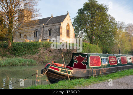 Heilig-kreuz-Kirche und Kanal Boot auf der Oxford canal Am frühen Morgen Frühling Sonnenlicht. Shipton auf Cherwell, Oxfordshire, England Stockfoto