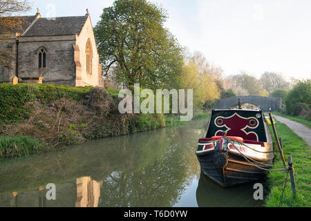 Heilig-kreuz-Kirche und Kanal Boot auf der Oxford canal Am frühen Morgen Frühling Sonnenlicht. Shipton auf Cherwell, Oxfordshire, England Stockfoto