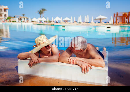 Senior paar Relaxen im Pool liegen auf eine Chaiselongue. Leute genießen Sommer Urlaub. Stockfoto