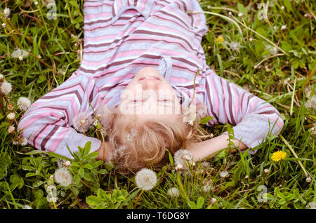 Adorable blonde Mädchen mit langen Haaren liegen unter weißen Löwenzahn Blumen Top View Stockfoto