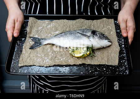 Hohen Winkel in der Nähe der Person, Backblech, mit Frische Dorade, Zitrone und Rosmarin Zweige. Stockfoto
