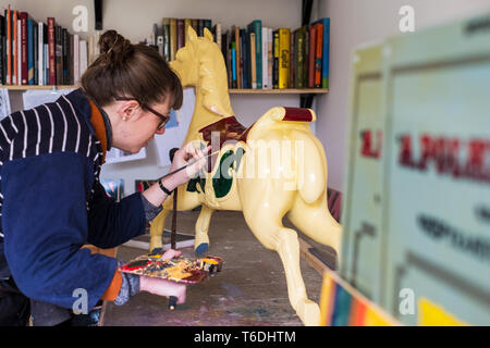 Frau, die in der Werkstatt, malen eine traditionelle Holz- Karussell Pferd von Merry-go-round. Stockfoto