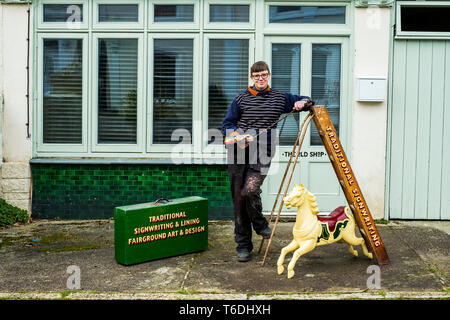 Frau signwriter und Handwerkerin holding Pinsel, Palette und Mahlstick, neben einer Leiter und kleinen Karussell Pferd. Stockfoto