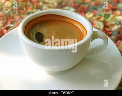 Heißer Schwarzer Kaffee in weisser Tasse serviert auf Blumenmuster Tischdecke Stockfoto