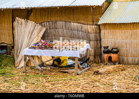 Souvenir für den Verkauf auf dem Holztisch und ein Teil von Haus aus Totora Schilfgras auf dem schwimmenden Uros Island auf dem Titicacasee in der Nähe der Stadt Puno Stockfoto