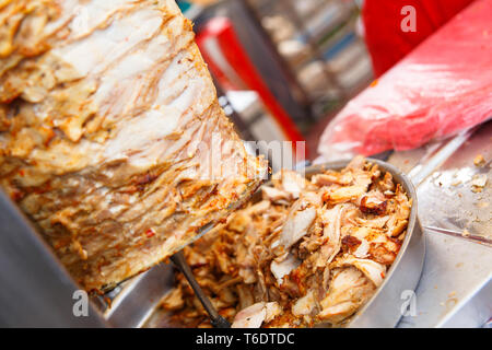 Gebratenes Fleisch schnitt von einem großen Stück Hühnerfleisch unter Fett kochen in einem Edelstahl Grill Maschine layered oft in und außerhalb von shawarma Stockfoto