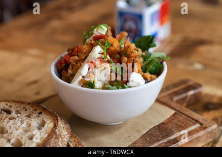 Ein linsensalat mit Ziegenkäse, butternut Kürbis und frischen Kräutern in einer weißen Schüssel, serviert mit sauerteigbrot Stockfoto