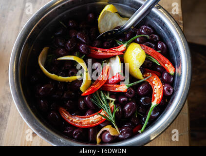 Schwarz, griechische Kalamata-oliven mariniert mit Chili, Zitronenschale und Rosmarin in eine silberne Schale Stockfoto