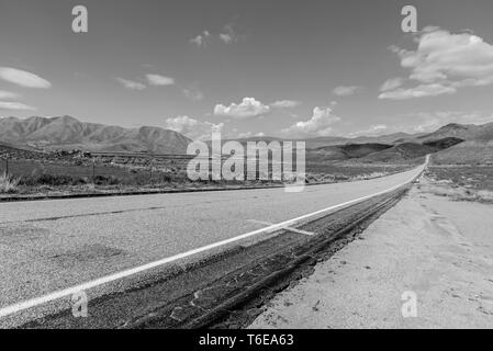 Schwarz und Weiß, lange gerade Straße durch Landschaft Berge laufen über unter Himmel mit weißen Wolken. Stockfoto