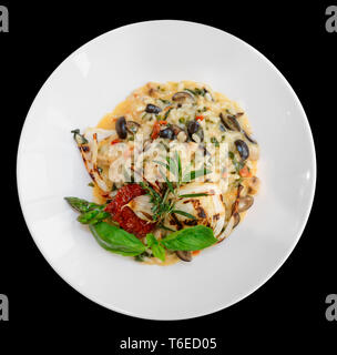 Risotto mit Tomaten und Kräutern in der Platte, auf schwarzem Hintergrund Stockfoto