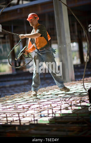 Männliche Bauarbeiter arbeiten mit einem Elektrowerkzeug auf einer Baustelle. Stockfoto