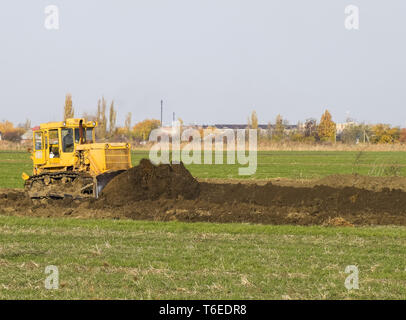 Die gelbe Traktor mit angehängtem grederom macht Boden ausrichten. Stockfoto