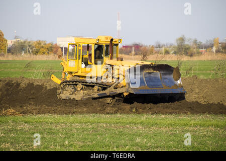 Die gelbe Traktor mit angehängtem grederom macht Boden ausrichten. Stockfoto