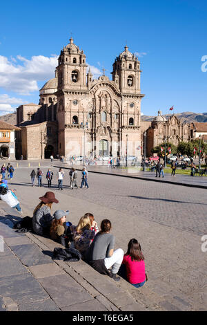 Gruppe von weissen Touristen Mädchen auf der Plaza de Armas oder Hauptplatz von Cusco sitzt und der wunderschöne Jesuitenkirche im Hintergrund, Cusco, Peru Stockfoto