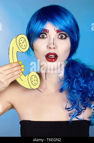 Porträt der jungen Frau in den komischen Pop art Make-up Stil. Frau in Blau Perücke auf blauem Hintergrund Anrufe über das Telefon Stockfoto