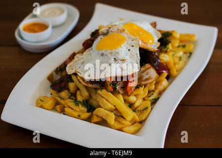 Pommes Frites mit zwei Eiern, Fleisch und Zwiebeln auf einem weißen Teller. Stockfoto