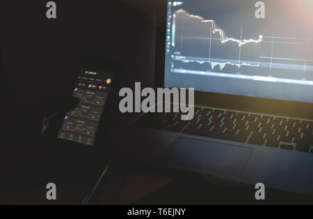 Wien Österreich April 26 2019, Tag Händler mobile Geräte. Forex day trader Holding Handy charts vor Computerbildschirmen suchen in dunklen Stockfoto