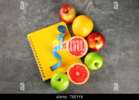 Früchte, Notebook und Maßband auf grauem Hintergrund. Ernährung Lebensmittel Stockfoto