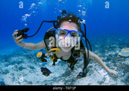 Frau Scuba Diver, mit einem blauen Maske, halten Sie die Regler auf der einen Seite und lächelnd an der Kamera auf einem tiefblauen Ozean, Insel Cozumel (Mexiko). Stockfoto