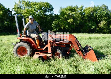 Hart arbeitende Frau Bauer stand auf und sprang nach der Fahrt ein Kubota orange Schlepper auf einem kleinen Bauernhof außerhalb Decorah, Iowa, USA Stockfoto