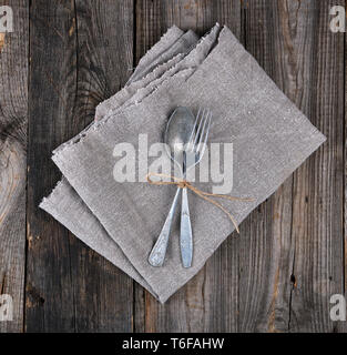 Alte Metall Gabel und Löffel mit einem braunen Seil auf einem grauen Leinen Servietten gebunden, Instrumente werden überschritten Stockfoto