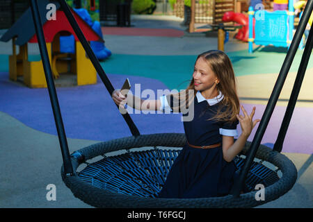 Jugendlich Mädchen Spaß haben auf dem Spielplatz nach der Schule. Freizeitaktivitäten. Schülerin geht auf Swing und nimmt selfie auf Handy. Glückliche Kindheit Stockfoto