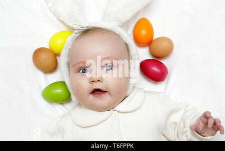 Neugeborene europäischen Baby Mädchen Junge mit Osterhasen Ohren 3 Monate alt unter gefärbten Eiern und Blumen Stockfoto