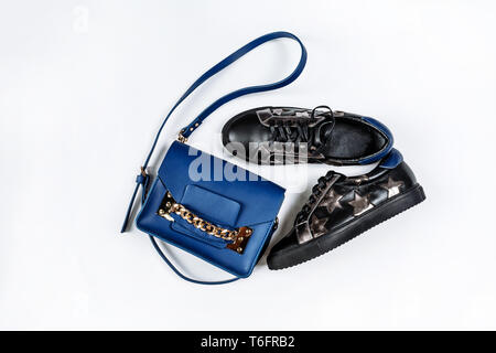Ein paar modische schwarze Leder Turnschuhe mit Silver Stars und eine blaue Tasche mit einer goldenen Kette auf weißem Hintergrund Stockfoto