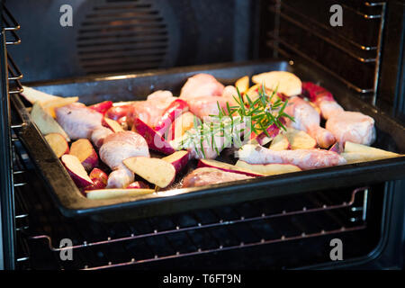 Raw organic Chicken Drumsticks und roten Kumara auf ein Backblech fertig gebraten, mit Rosmarin. Gewürzt mit geräuchertem Salz und weißer Pfeffer. Stockfoto