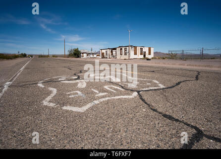 Route 66 mit Risse und gebrochene Pflaster mit einem verlassenen Gebäude, das am Straßenrand im Hintergrund. Stockfoto