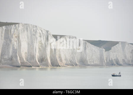 Cuckmere Haven, East Sussex, UK. Mai, 2019. Ein kleines Fischerboot arbeiten an der Basis der legendären sieben Schwestern Kreidefelsen an bewölkten Tag, in der Nähe von Eastbourne, Sussex, leicht auf eine flache diesigen Tag. Credit: Peter Cripps/Alamy leben Nachrichten Stockfoto