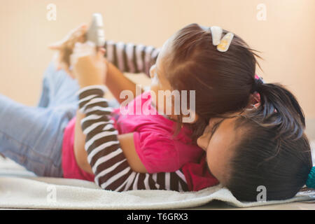 Zwei süße Indischen kleine Geschwister kämpfen für Mobiltelefon, Krabbeln an einander auf dem Bett. Stockfoto