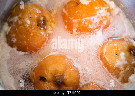 Nahaufnahme von Quitten simmering in einem großen Edelstahl Topf in einem Zuckersirup. Sie haben Rubinrot aus der Tannine im Obst. Stockfoto